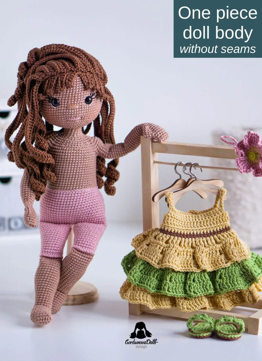 Crochet doll Emily standing next to a hanger with her removable crochet dress - made using the amigurumi doll pattern