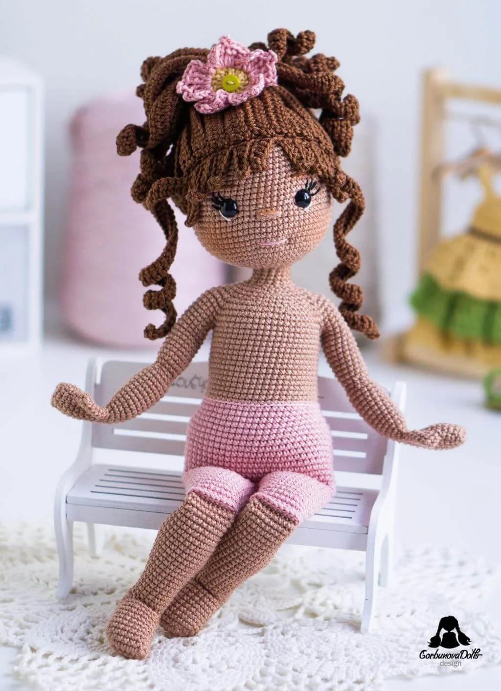 Crochet doll Emily sitting on a bench without her removable outfit – made using the amigurumi doll pattern